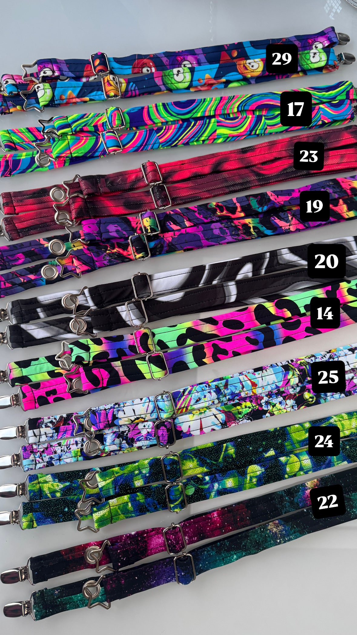 A top view of different colorful Magic Utility Strap sets! Wrapped in UV reactive soft spandex and tricked out with a grommet and extra silver attachment hardware to wear your jacket like a backpack.
